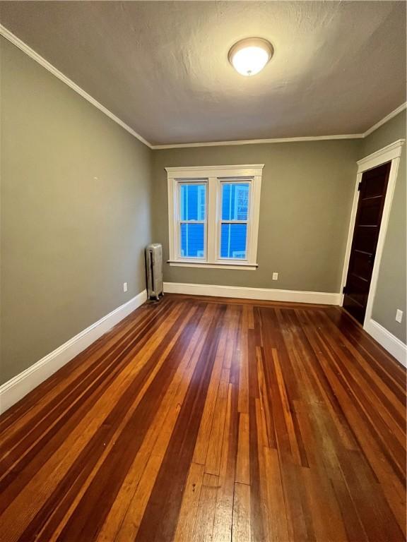 unfurnished room featuring dark hardwood / wood-style flooring, radiator heating unit, and crown molding