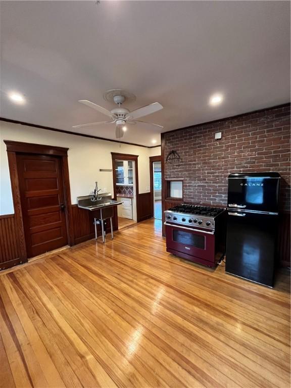 kitchen with a breakfast bar, black refrigerator, high end stainless steel range, ceiling fan, and light wood-type flooring