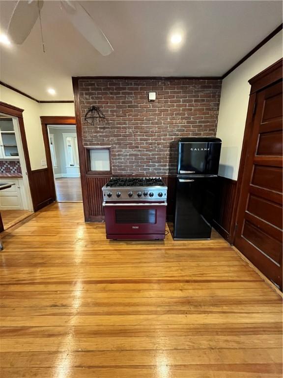 kitchen featuring black fridge, light wood-type flooring, high end stainless steel range oven, and ornamental molding