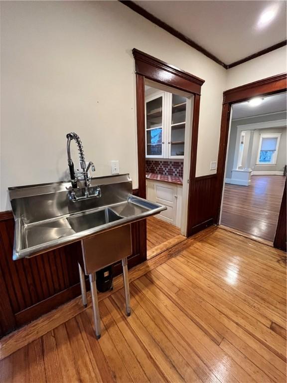 interior space with decorative backsplash, ornamental molding, stainless steel counters, sink, and light hardwood / wood-style floors