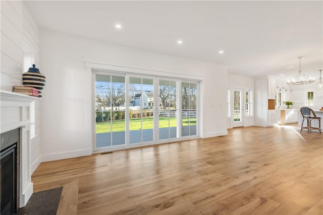 unfurnished living room featuring a notable chandelier and light wood-type flooring