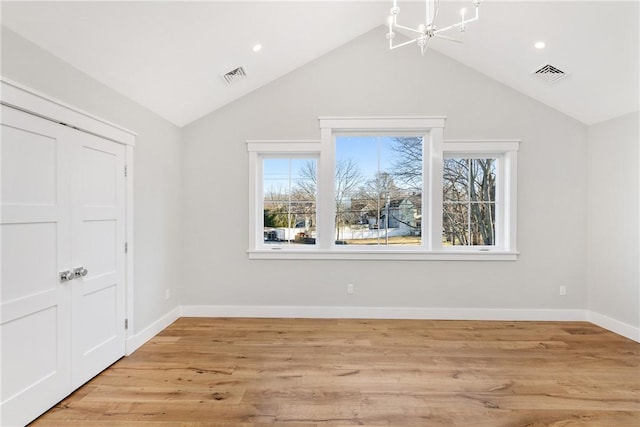 unfurnished bedroom with multiple windows, lofted ceiling, light hardwood / wood-style floors, and an inviting chandelier