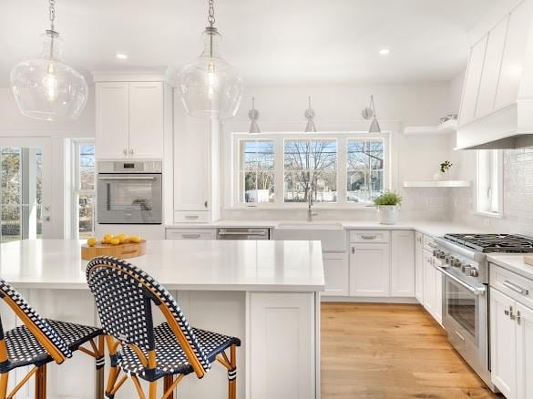 kitchen featuring white cabinetry, appliances with stainless steel finishes, decorative light fixtures, and custom range hood