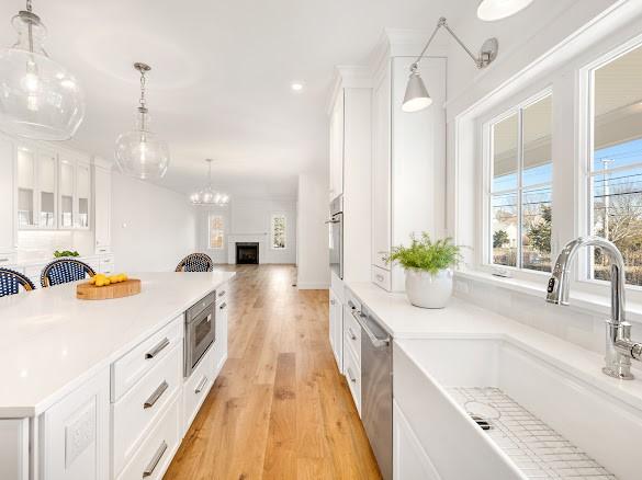 kitchen with sink, white cabinetry, hanging light fixtures, stainless steel appliances, and light hardwood / wood-style floors