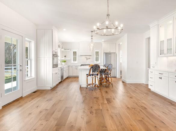 kitchen with a kitchen island, a breakfast bar, appliances with stainless steel finishes, white cabinets, and light hardwood / wood-style flooring