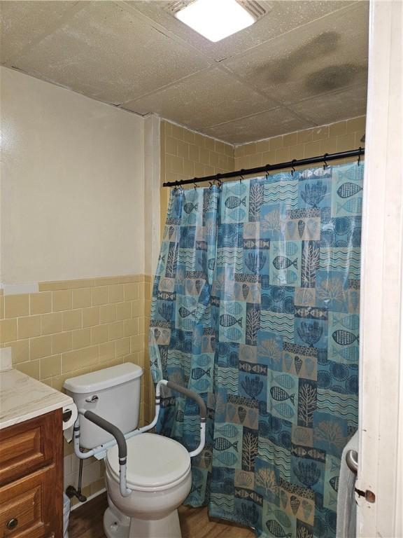 bathroom with vanity, hardwood / wood-style flooring, a shower with shower curtain, toilet, and tile walls