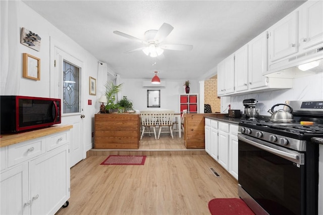 kitchen featuring white cabinets, an AC wall unit, light hardwood / wood-style flooring, gas range, and ceiling fan