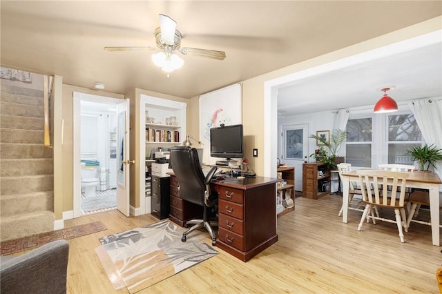 home office with built in shelves, ceiling fan, and light hardwood / wood-style flooring