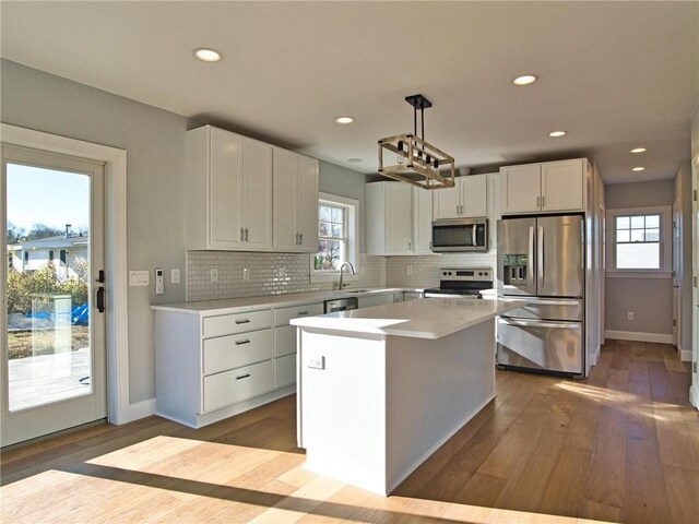 kitchen with hanging light fixtures, white cabinets, stainless steel appliances, and a kitchen island