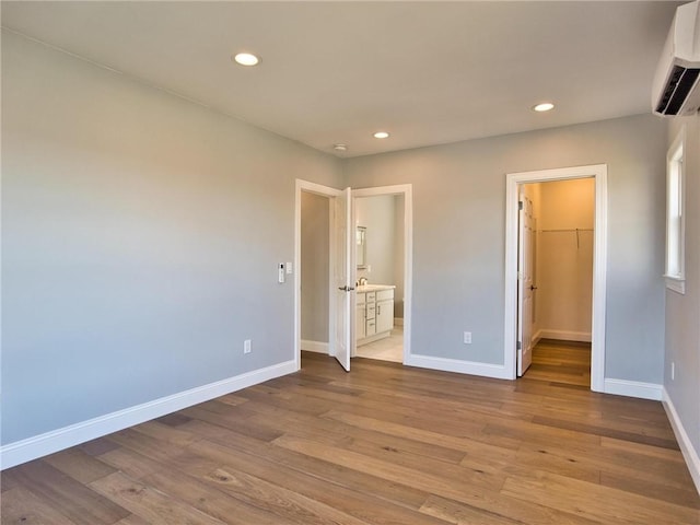 unfurnished bedroom with recessed lighting, wood finished floors, baseboards, a wall mounted AC, and a walk in closet