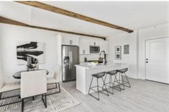 kitchen featuring beam ceiling, white cabinetry, stainless steel appliances, a kitchen breakfast bar, and a center island with sink