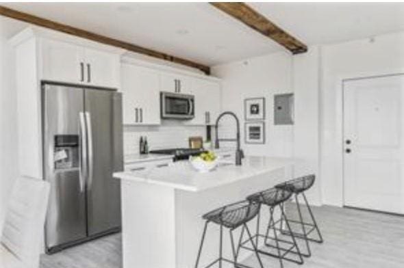 kitchen featuring a center island with sink, light hardwood / wood-style flooring, a kitchen bar, white cabinetry, and stainless steel appliances