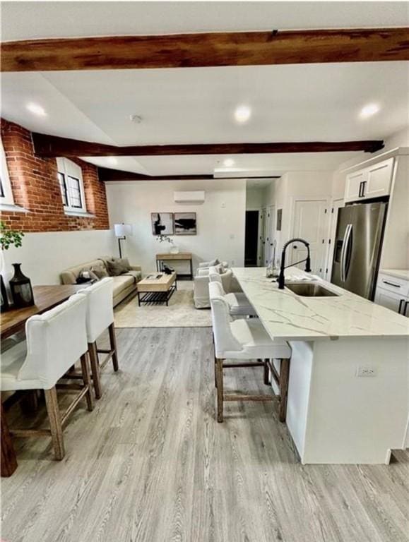 interior space with beam ceiling, an AC wall unit, sink, and light hardwood / wood-style flooring