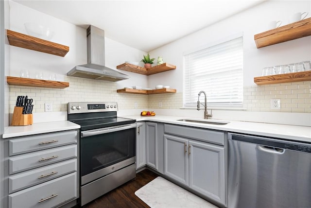 kitchen featuring gray cabinetry, sink, stainless steel appliances, and wall chimney range hood