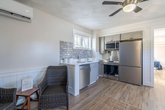 kitchen with gray cabinetry, stainless steel appliances, a wall mounted air conditioner, tasteful backsplash, and light wood-type flooring