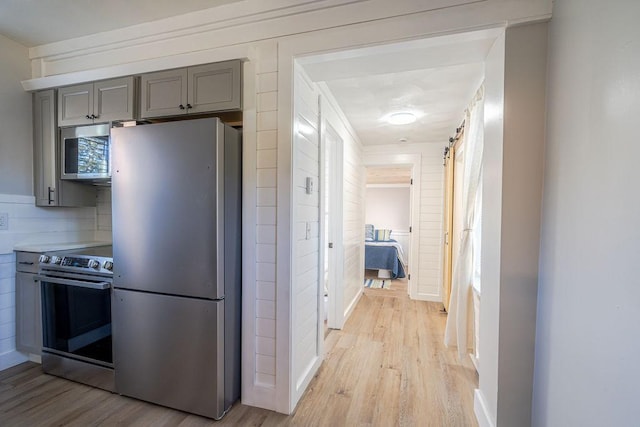 kitchen with appliances with stainless steel finishes, backsplash, gray cabinetry, a barn door, and light hardwood / wood-style flooring