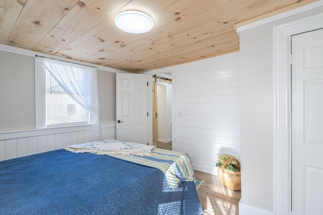 bedroom featuring wood-type flooring, a barn door, wooden walls, and wooden ceiling