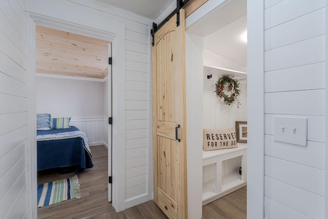 corridor with a barn door, light hardwood / wood-style floors, vaulted ceiling, and crown molding