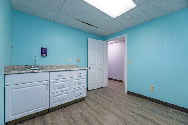 interior space featuring light hardwood / wood-style flooring, white cabinets, a drop ceiling, and sink