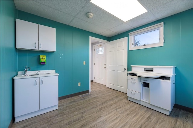 kitchen with white cabinetry, a drop ceiling, sink, and light wood-type flooring