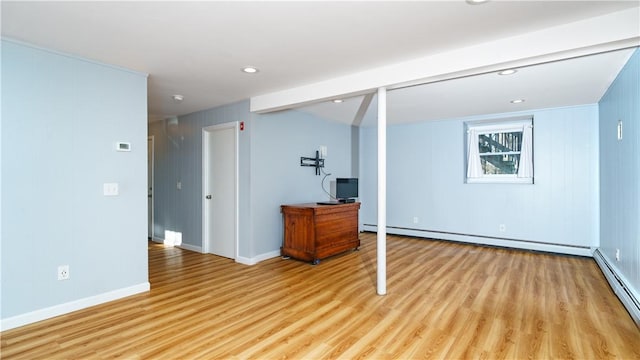 basement with wooden walls, light hardwood / wood-style floors, and a baseboard heating unit