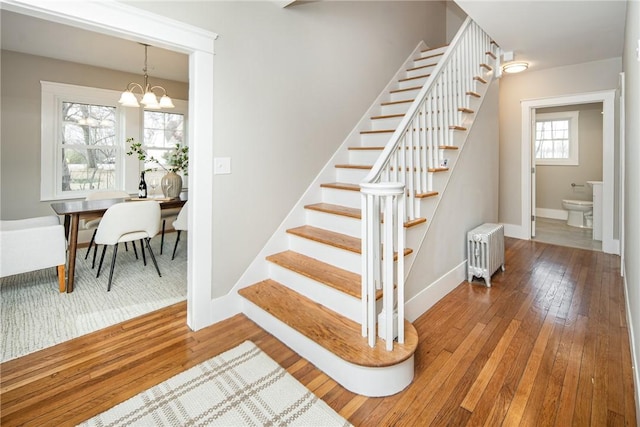 stairway featuring wood-type flooring, radiator, and a notable chandelier