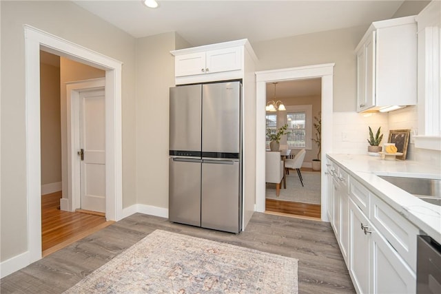 kitchen featuring backsplash, white cabinets, appliances with stainless steel finishes, light hardwood / wood-style floors, and light stone counters