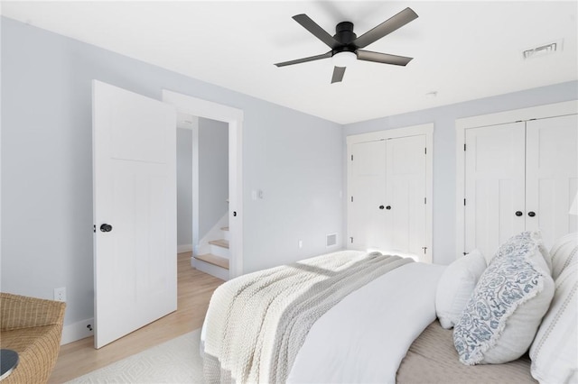 bedroom with ceiling fan, light hardwood / wood-style floors, and two closets