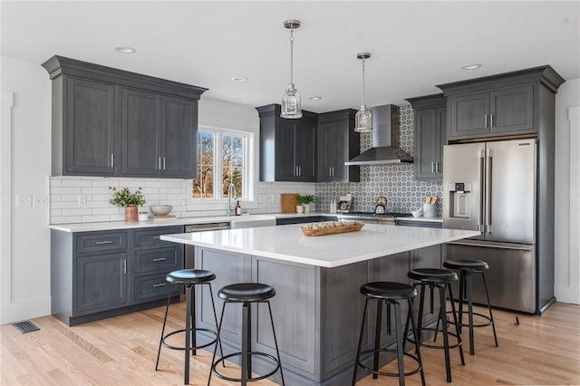 kitchen with a kitchen bar, a center island, stainless steel appliances, and wall chimney range hood