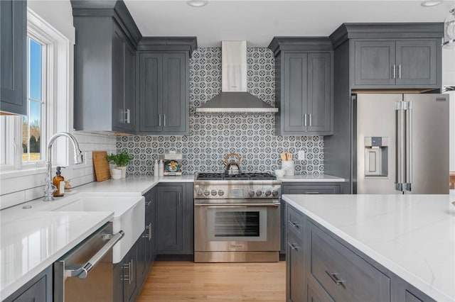 kitchen with premium appliances, light stone counters, a wealth of natural light, and wall chimney exhaust hood