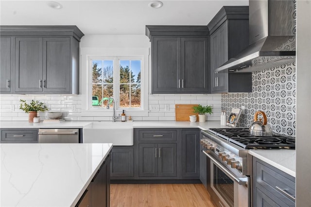 kitchen with wall chimney range hood, sink, decorative backsplash, appliances with stainless steel finishes, and light stone counters