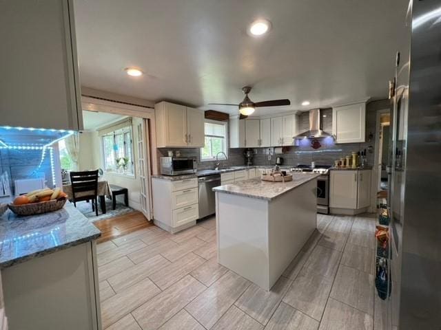 kitchen featuring sink, a center island, wall chimney exhaust hood, white cabinets, and appliances with stainless steel finishes