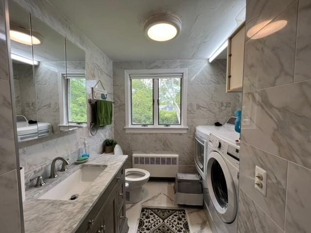 bathroom featuring washer and clothes dryer, vanity, toilet, tile walls, and radiator heating unit