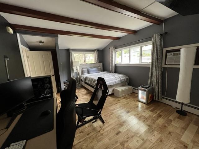 bedroom featuring vaulted ceiling with beams, an AC wall unit, and light hardwood / wood-style flooring