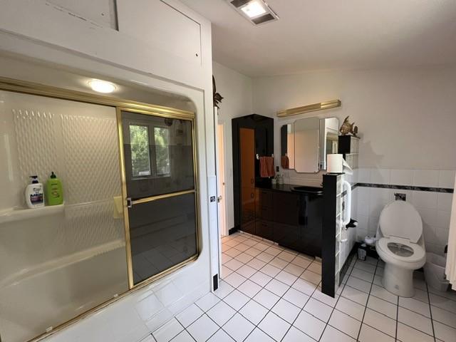 bathroom with tile patterned floors, enclosed tub / shower combo, tile walls, and toilet