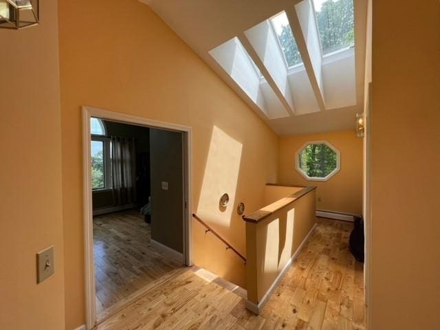 hall with baseboard heating, lofted ceiling with skylight, and light wood-type flooring