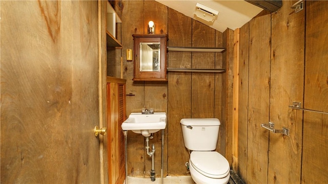 bathroom featuring toilet, sink, and wooden walls