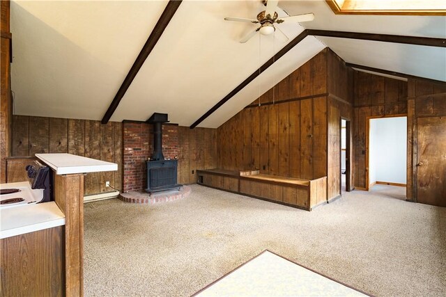 unfurnished living room with carpet flooring, ceiling fan, lofted ceiling with beams, a wood stove, and wood walls