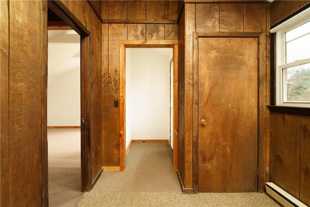 hallway with light carpet, a baseboard heating unit, and wood walls