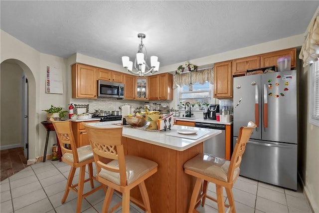 kitchen with a kitchen bar, appliances with stainless steel finishes, sink, light tile patterned floors, and a center island