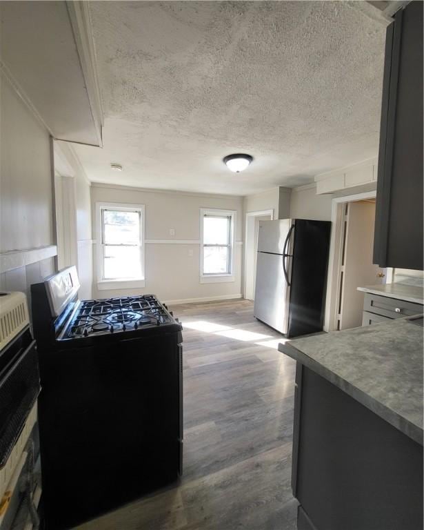 kitchen with stainless steel fridge, hardwood / wood-style flooring, a textured ceiling, and black range with electric cooktop