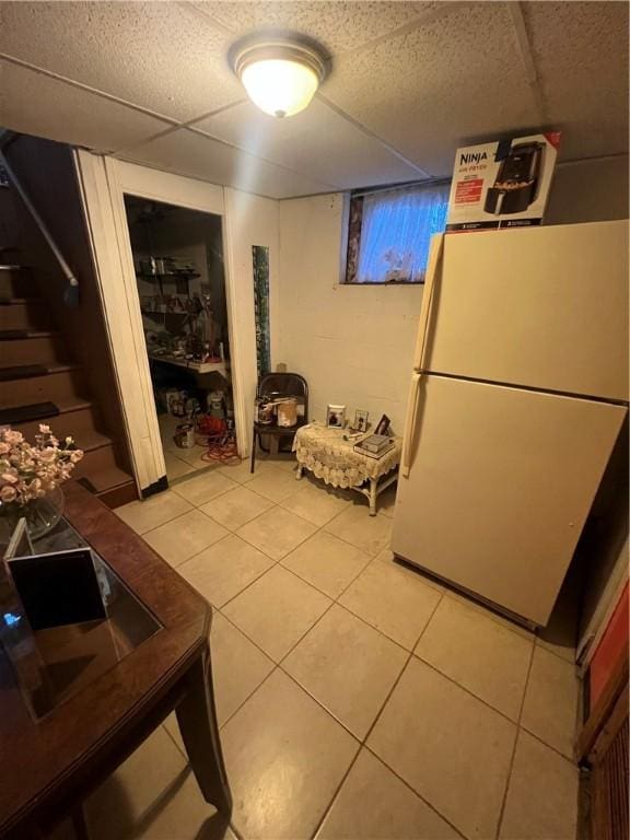 basement with a paneled ceiling, white refrigerator, and light tile patterned flooring