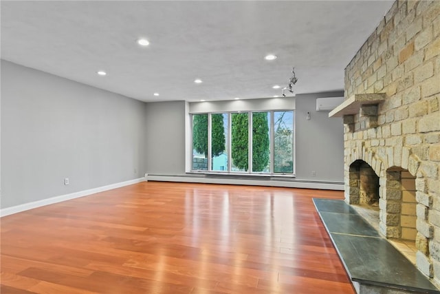 unfurnished living room featuring hardwood / wood-style floors, a large fireplace, a baseboard radiator, and a wall mounted air conditioner