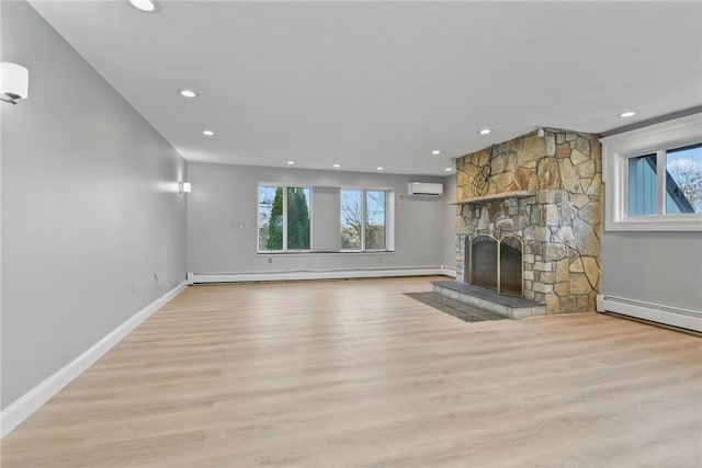 unfurnished living room featuring a baseboard radiator, a stone fireplace, a wall mounted AC, and light hardwood / wood-style floors