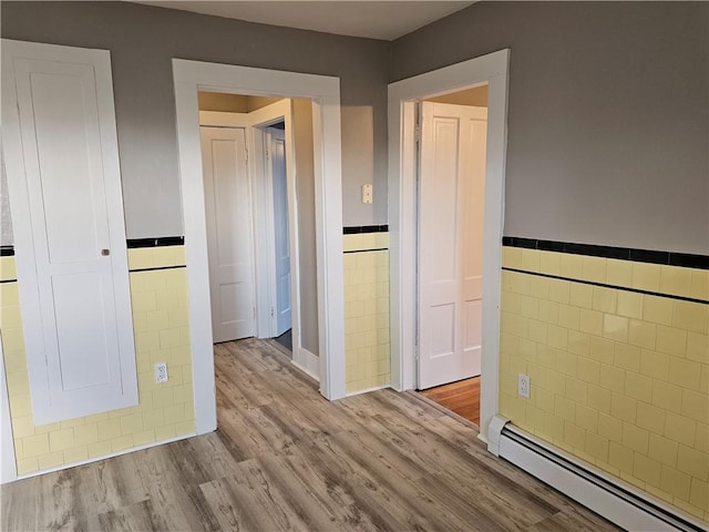 interior space with baseboard heating, light hardwood / wood-style flooring, and tile walls