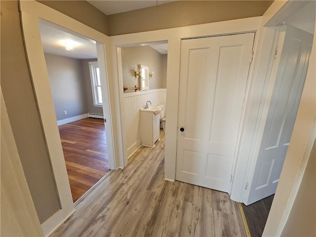 corridor with light wood-type flooring and a baseboard heating unit