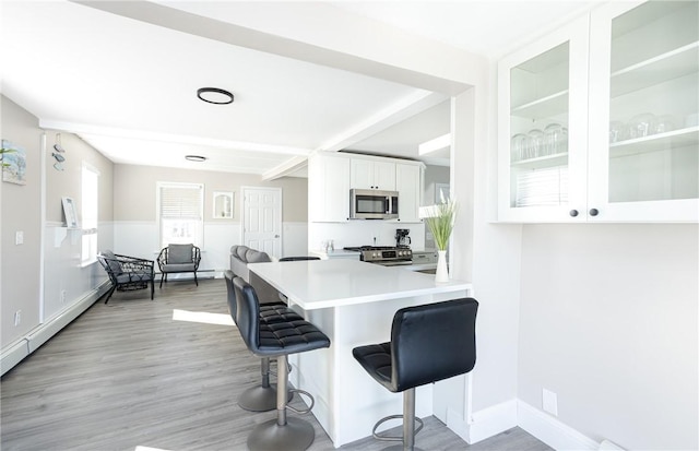 kitchen with kitchen peninsula, light hardwood / wood-style floors, a kitchen bar, white cabinets, and appliances with stainless steel finishes