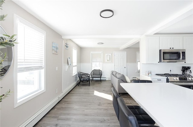 kitchen with white cabinets, beam ceiling, light hardwood / wood-style floors, and stainless steel appliances