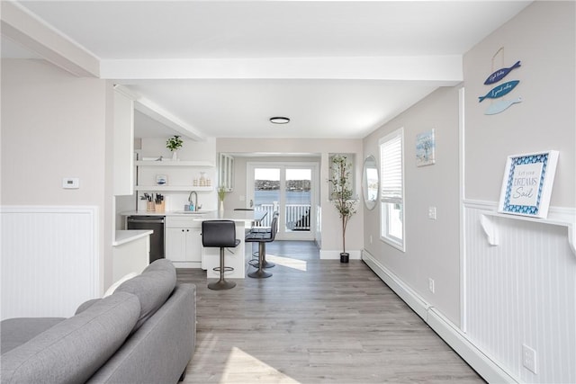 living room with baseboard heating, sink, and light hardwood / wood-style flooring