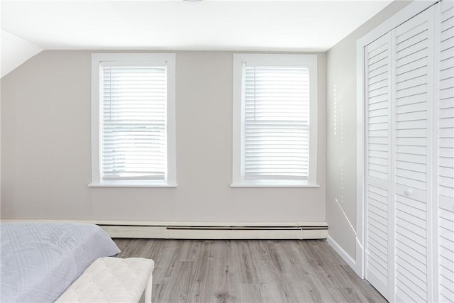 unfurnished bedroom featuring vaulted ceiling, light wood-type flooring, baseboard heating, and multiple windows